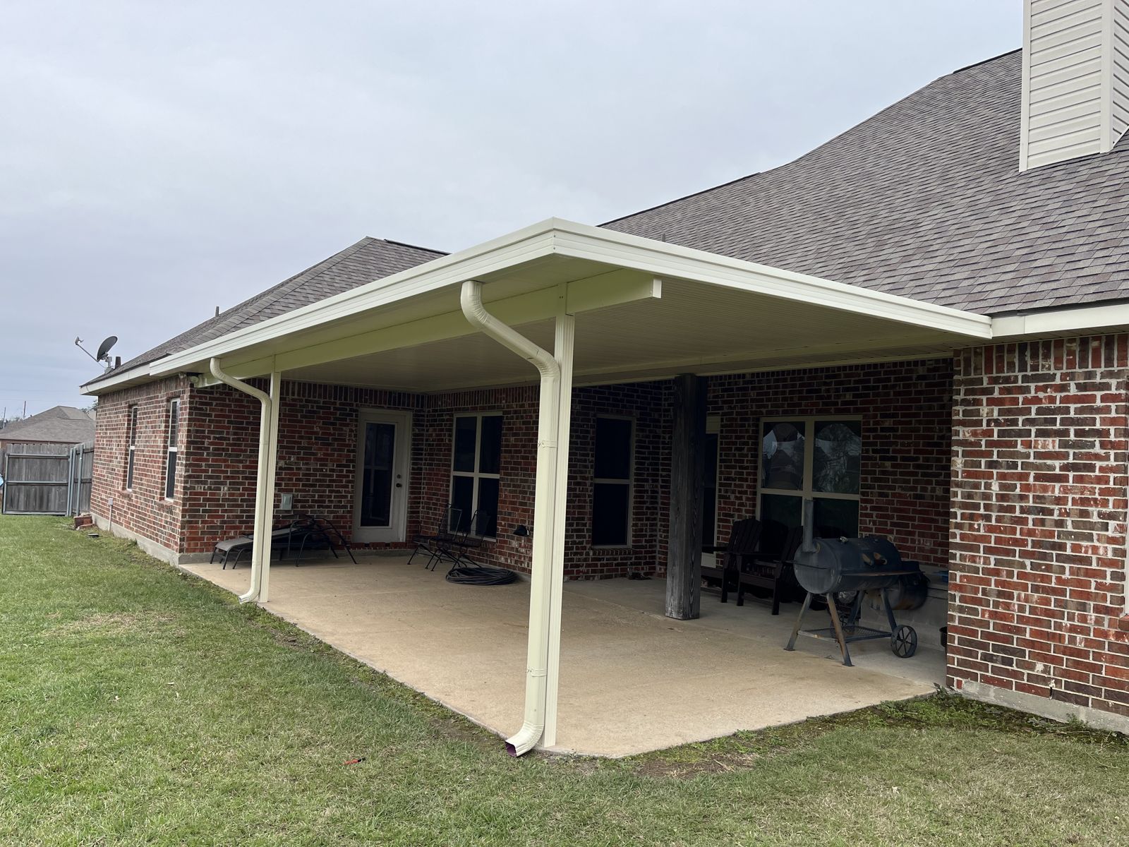 White aluminum patio cover with downspouts along the back of a brick home