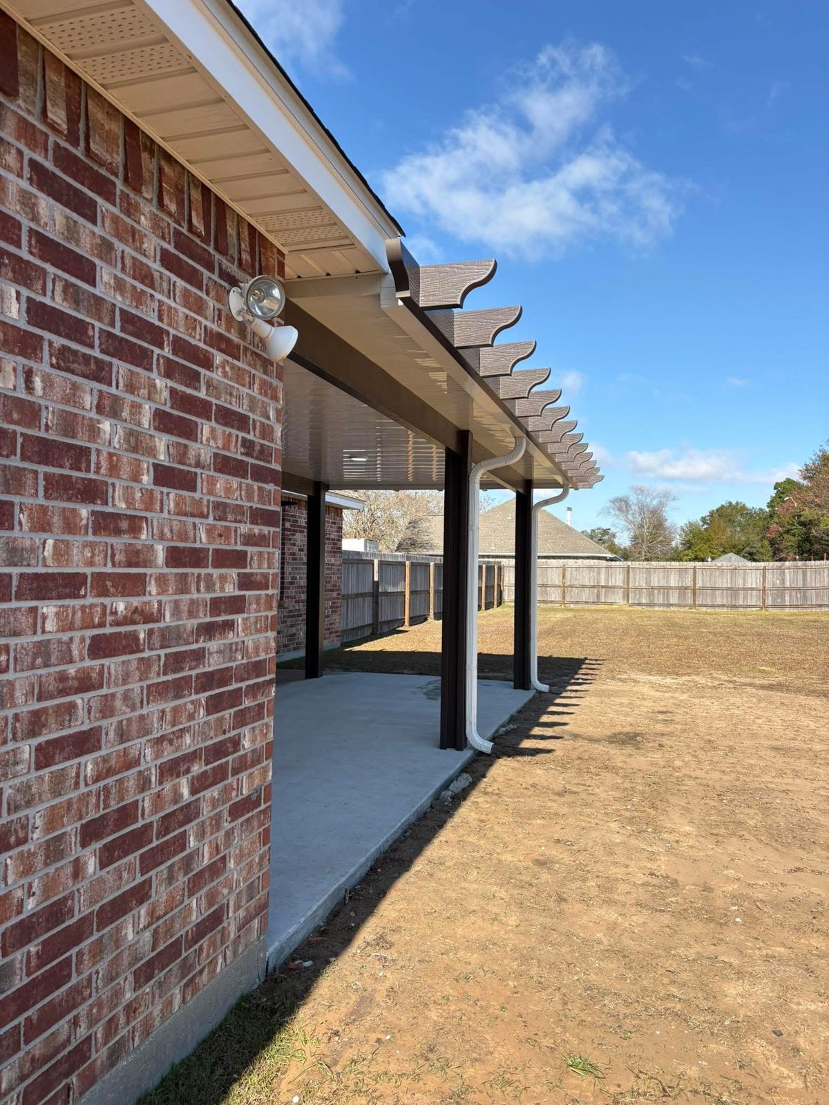Brown pergola-style patio cover along a brick home