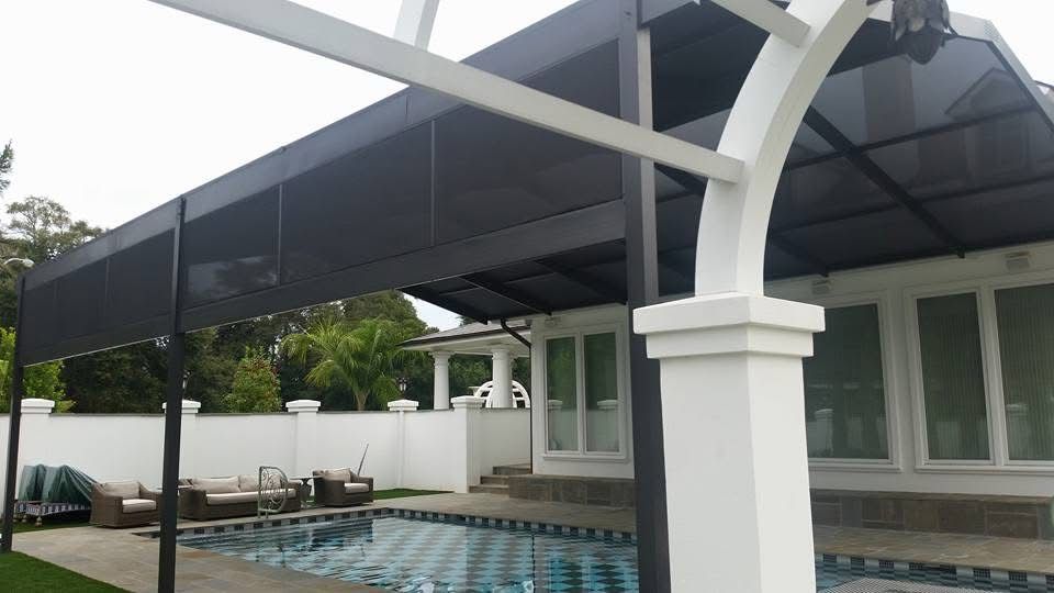 Dark patio cover with shade panels and a white arch over a pool