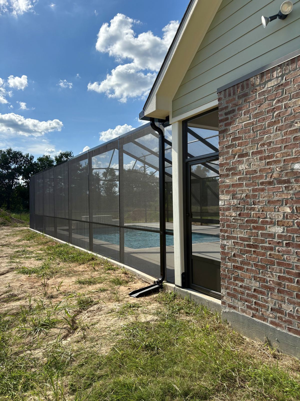 Side wall of a pool screen enclosure attached to a brick home