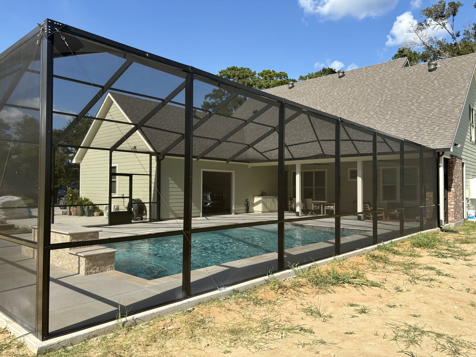 Dark bronze pool screen enclosure attached to a home beside a covered patio