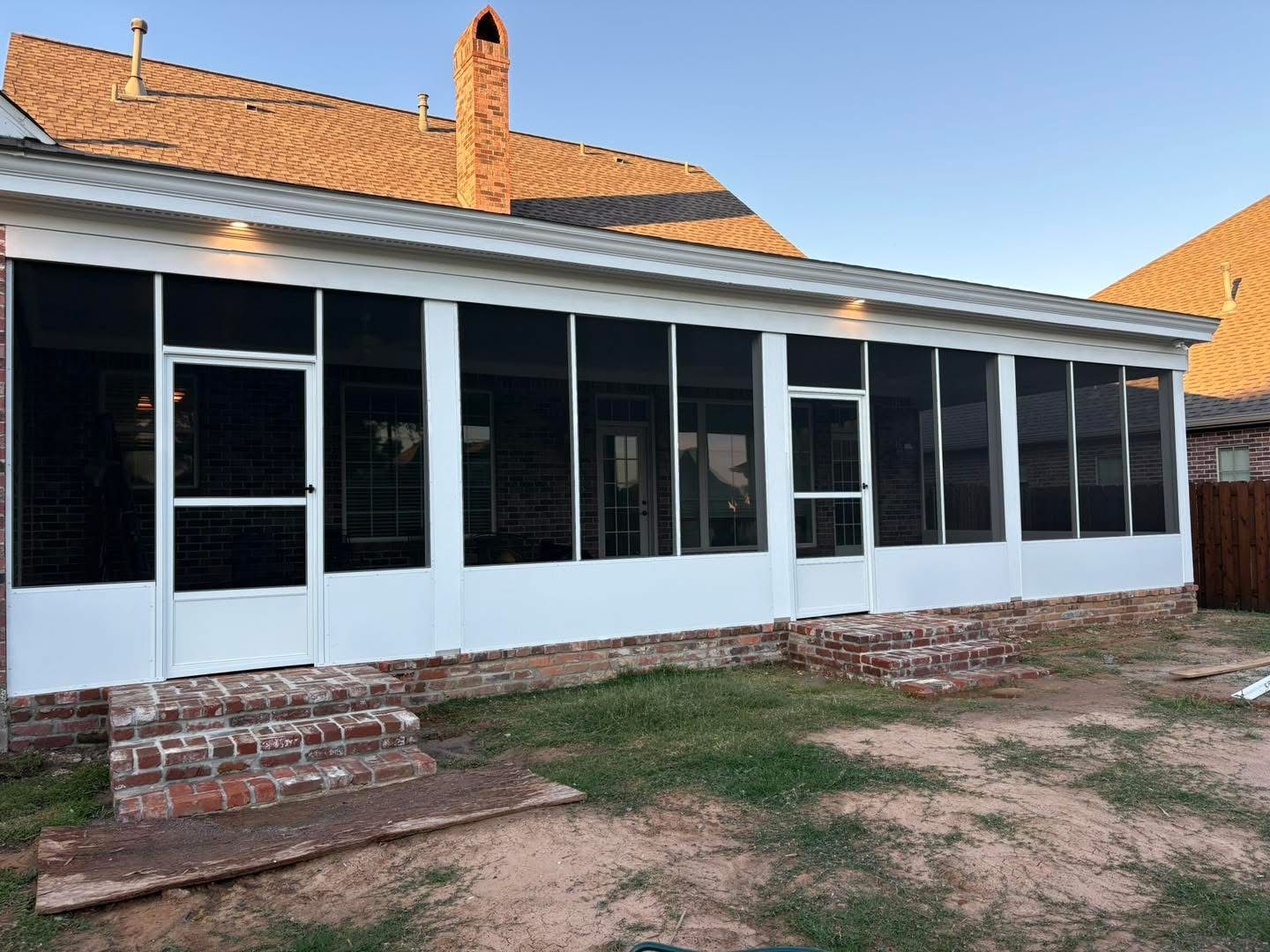 White screened porch with two screen doors and brick steps