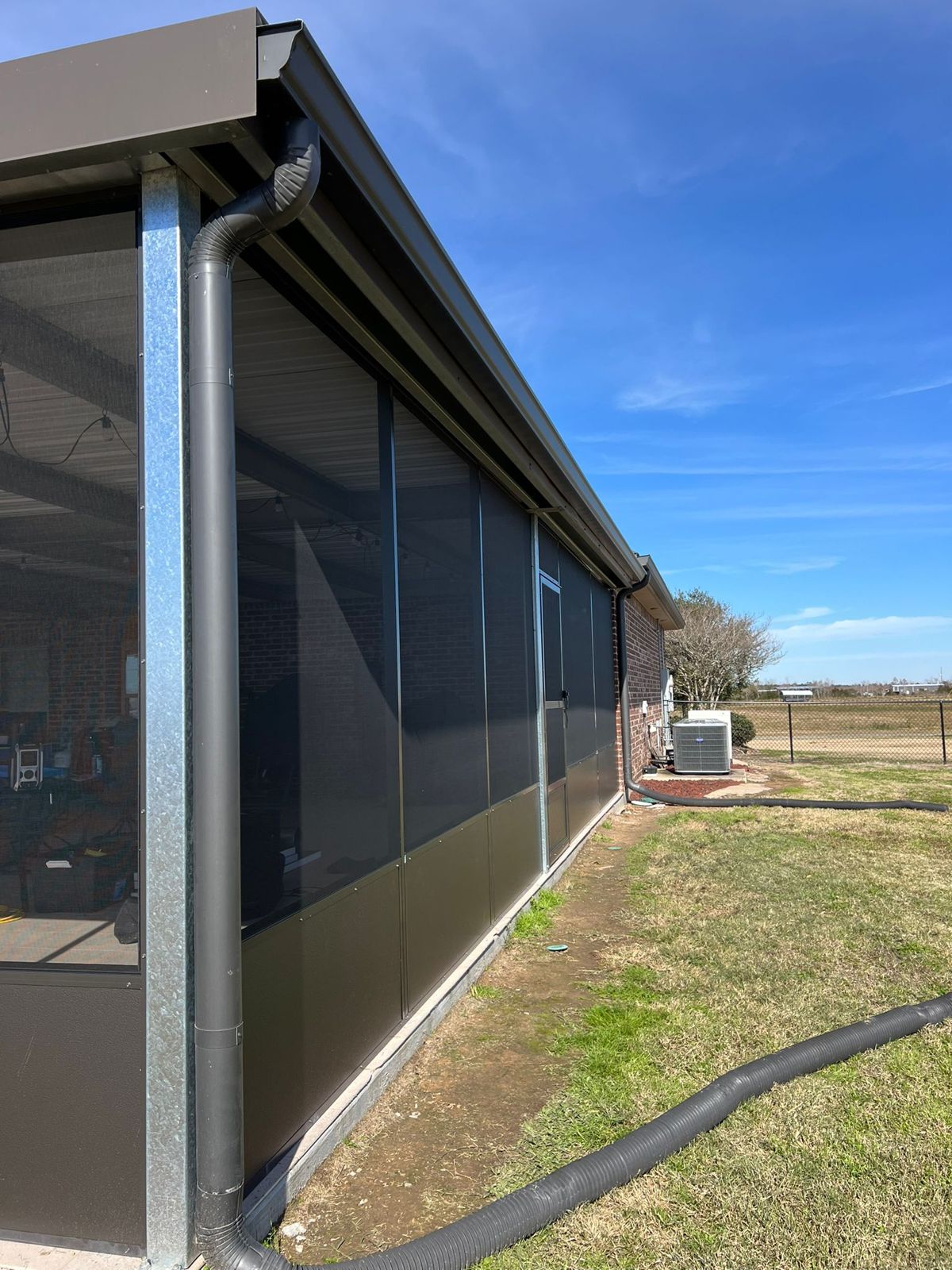 Exterior of a long screen enclosure with dark kick panels and downspout
