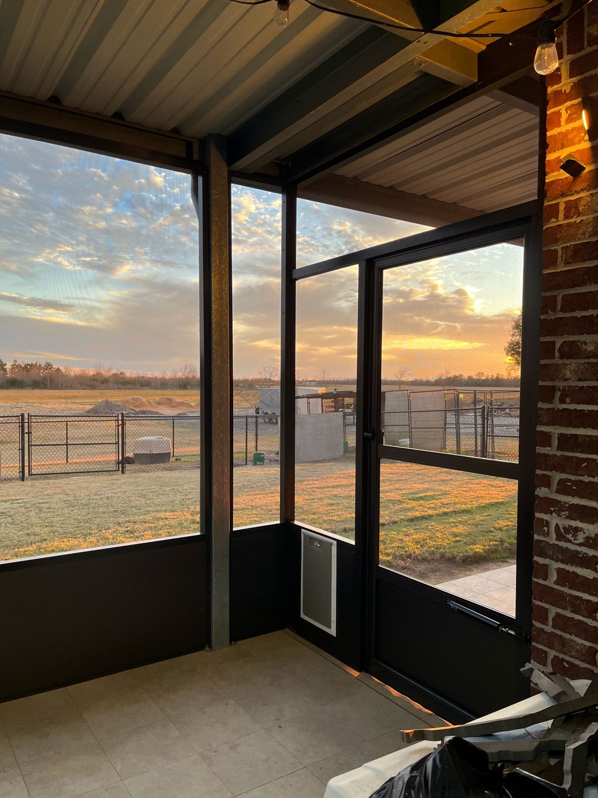 Screen room corner with screen door and pet door beside brick wall