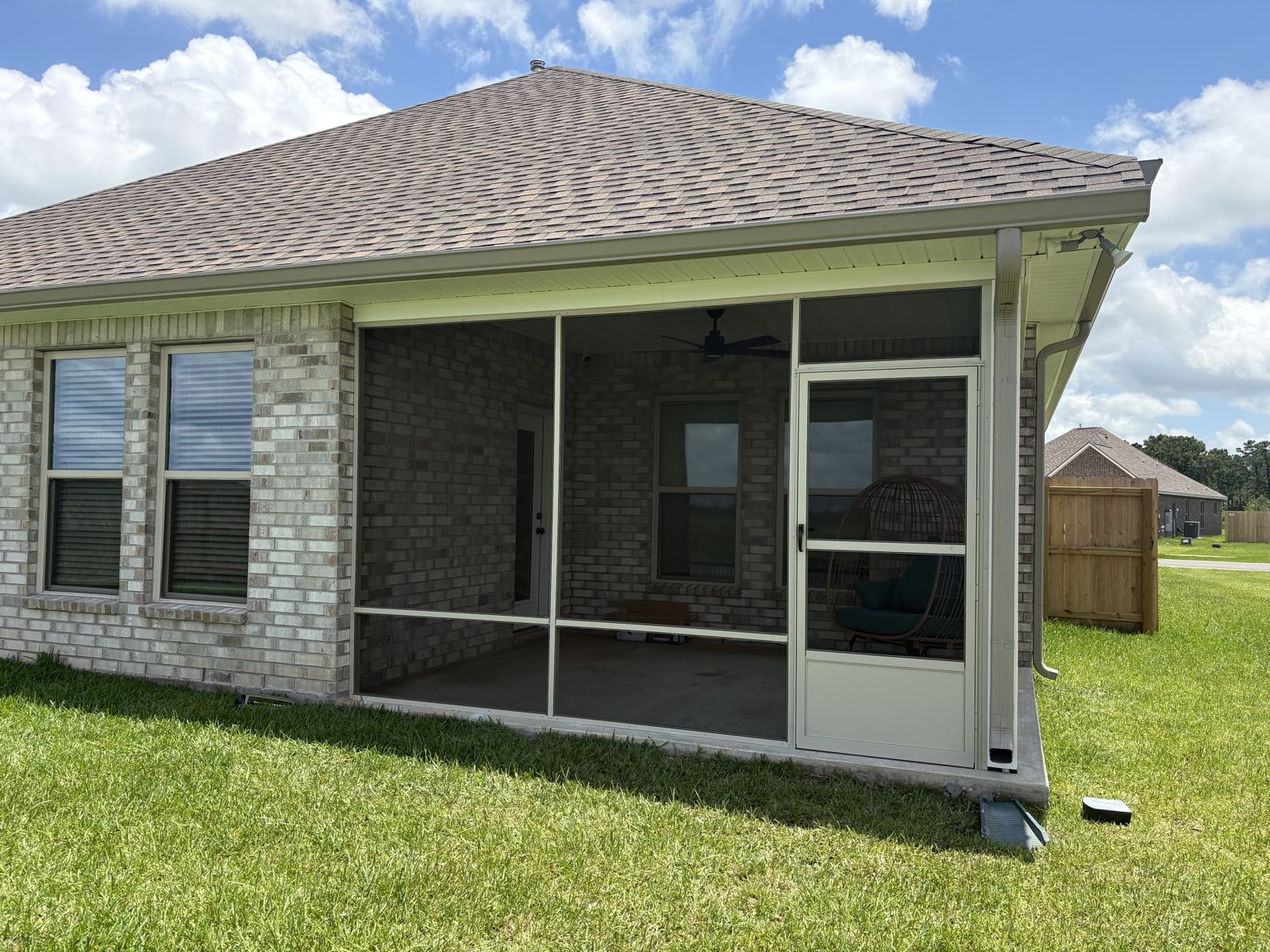 Beige screen room with ceiling fan and screen door on a brick home