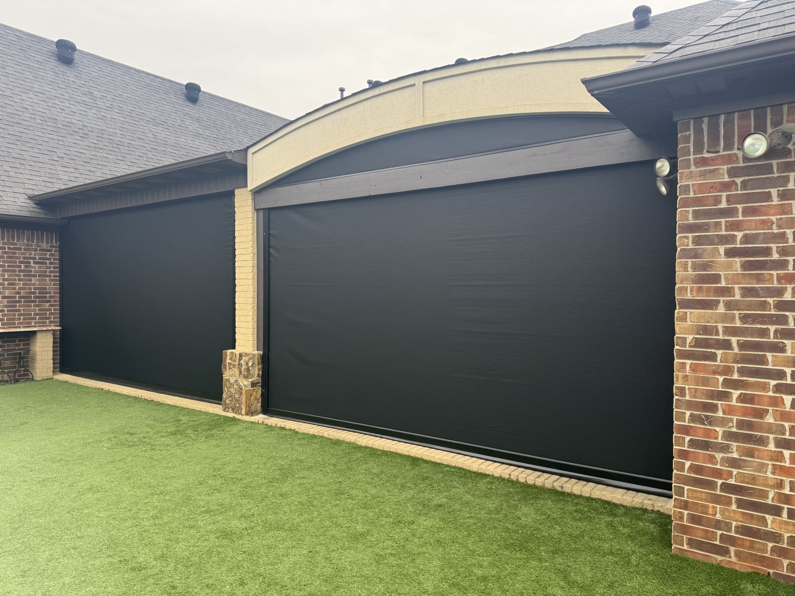 Black motorized shades lowered on a brick home's back patio openings