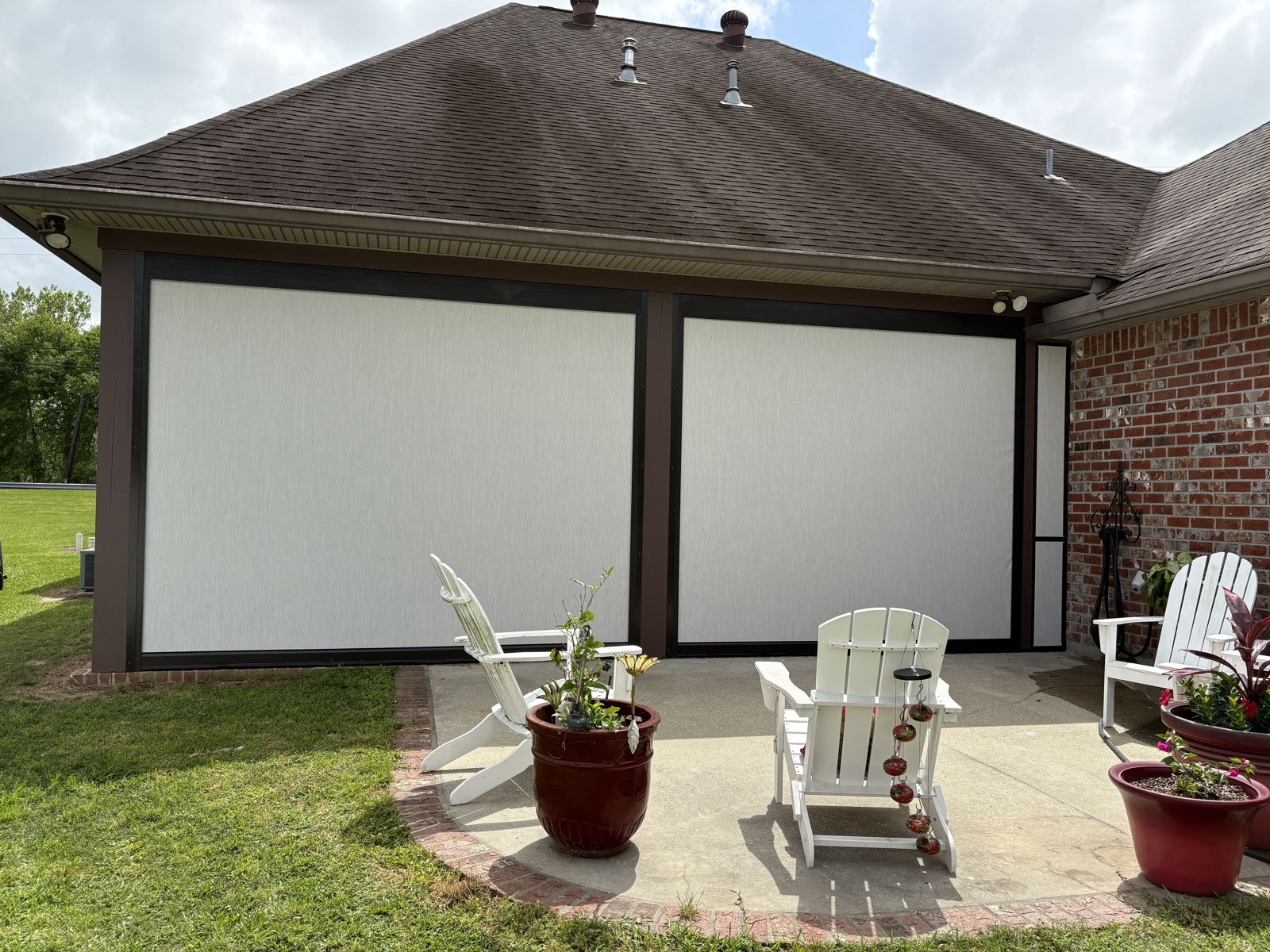 Cream roller shades lowered on a brick home back patio with outdoor chairs